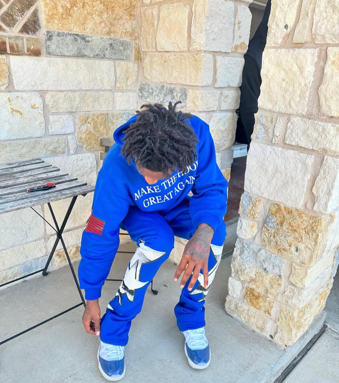 youtuber lil loaded wearing a blue hoodie with the text 'MAKE THE HOOD GREAT AGAIN' on it,  paired with matching blue pants with a graphic design, standing outdoors. from neighborhood supplier